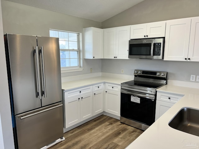 kitchen with dark wood-type flooring, appliances with stainless steel finishes, vaulted ceiling, and white cabinets