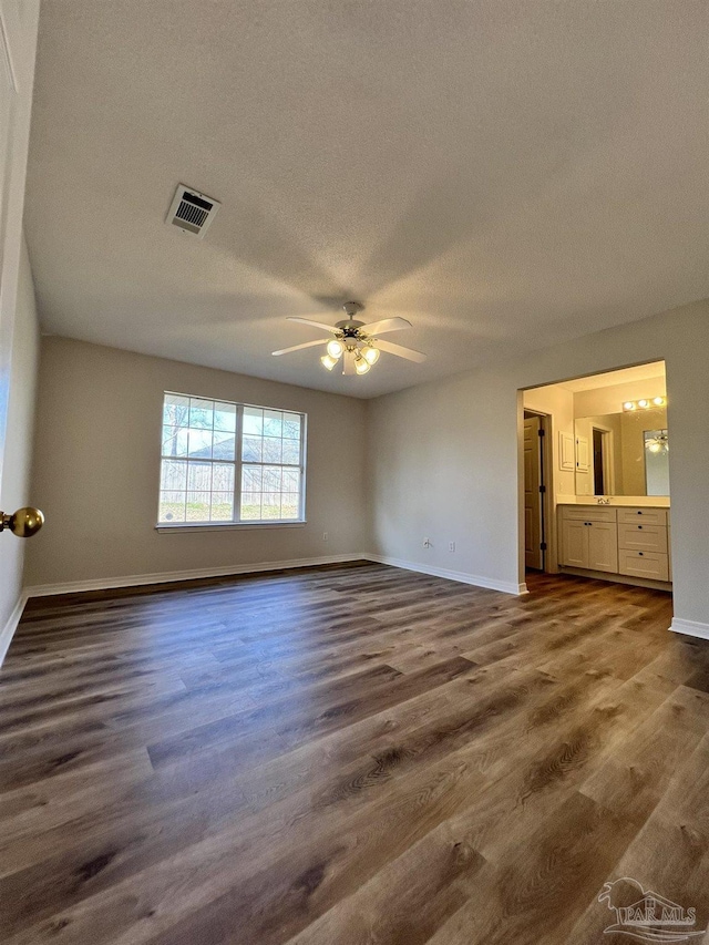 unfurnished bedroom featuring dark wood-type flooring, ceiling fan, connected bathroom, and a textured ceiling