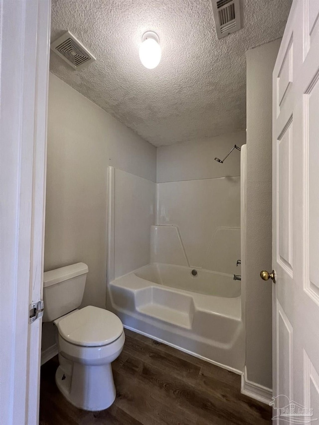 bathroom featuring hardwood / wood-style floors, washtub / shower combination, a textured ceiling, and toilet