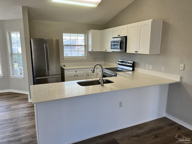 kitchen with appliances with stainless steel finishes, white cabinetry, lofted ceiling, sink, and kitchen peninsula