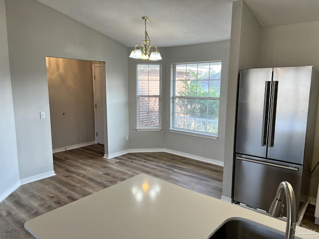 kitchen featuring wood-type flooring, stainless steel fridge, decorative light fixtures, and vaulted ceiling