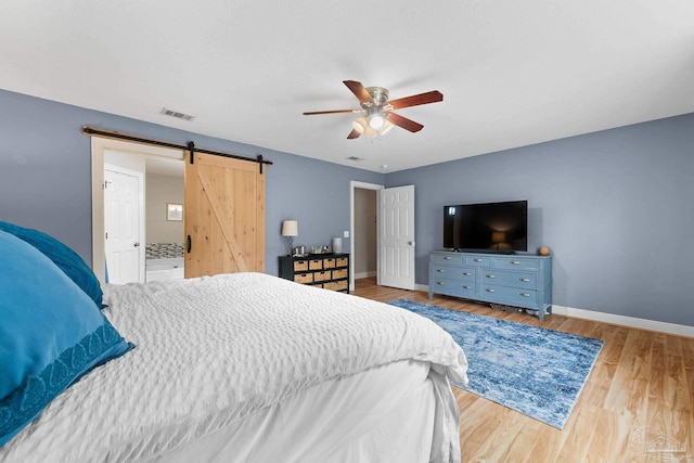 bedroom featuring a barn door, hardwood / wood-style flooring, and ceiling fan