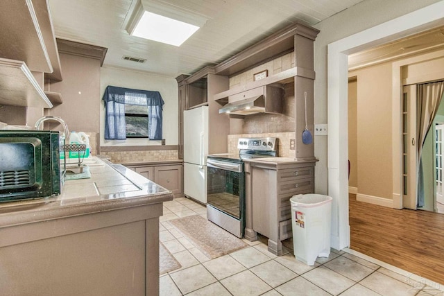 kitchen featuring range hood, white refrigerator, backsplash, stainless steel range with electric stovetop, and light tile patterned flooring