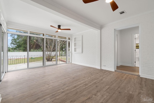 unfurnished living room with ceiling fan, hardwood / wood-style floors, brick wall, and a wall of windows