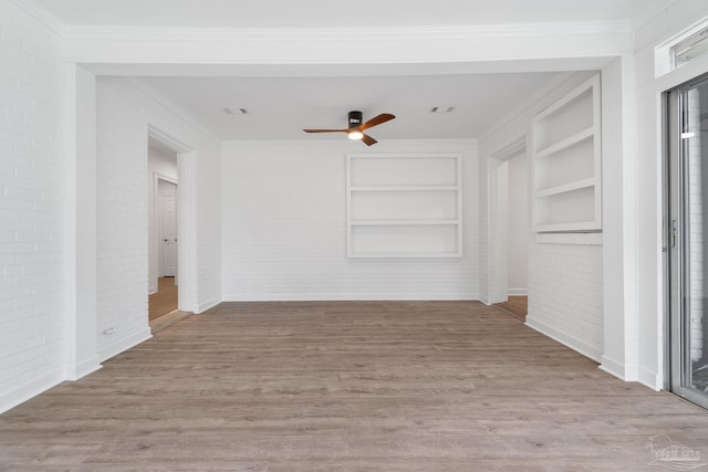 unfurnished living room with ceiling fan, built in features, brick wall, crown molding, and light hardwood / wood-style floors