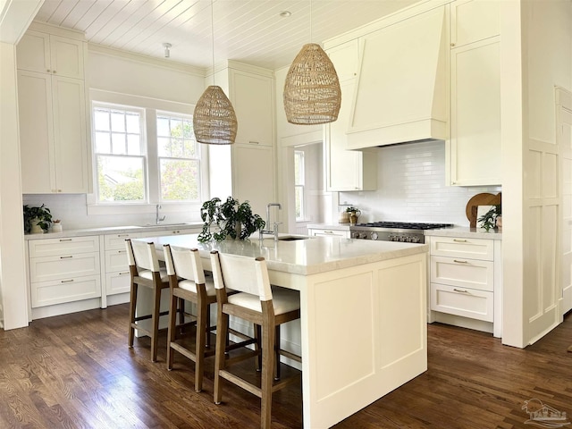 kitchen featuring pendant lighting, sink, tasteful backsplash, an island with sink, and custom range hood