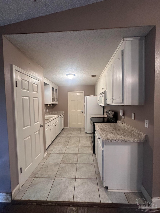kitchen featuring a textured ceiling, white appliances, white cabinets, light countertops, and light tile patterned floors