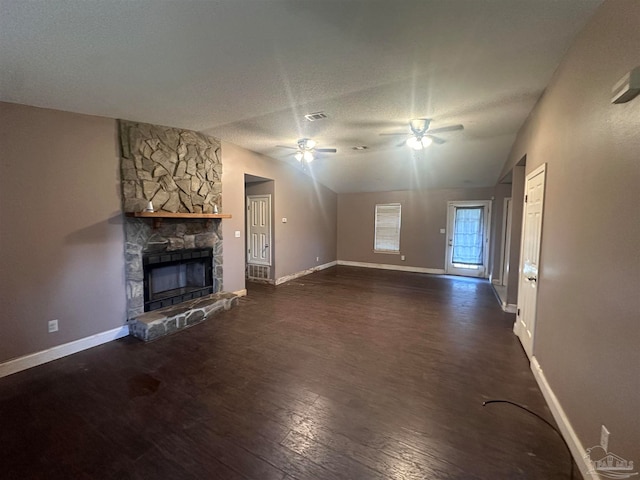 unfurnished living room featuring visible vents, a textured ceiling, wood finished floors, a stone fireplace, and ceiling fan