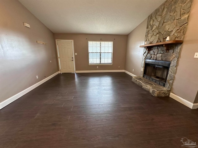 unfurnished living room featuring baseboards, dark wood-style floors, vaulted ceiling, a textured ceiling, and a stone fireplace