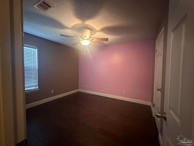 empty room with dark wood-style floors, visible vents, baseboards, and ceiling fan