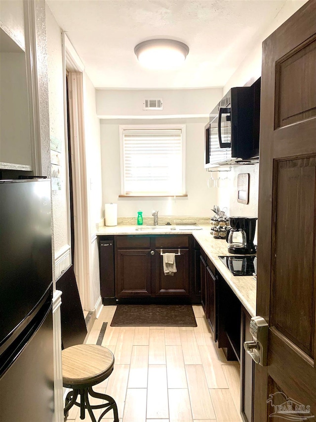 kitchen with sink, dark brown cabinets, black electric cooktop, and light hardwood / wood-style flooring