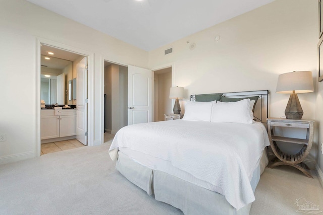 bedroom with ensuite bathroom and light carpet