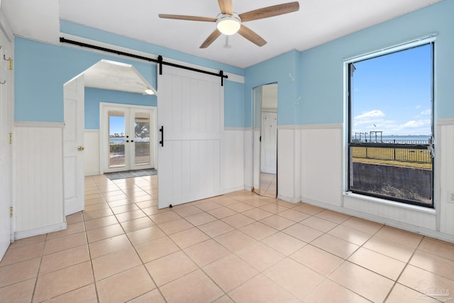 spare room with french doors, light tile patterned floors, a barn door, and ceiling fan