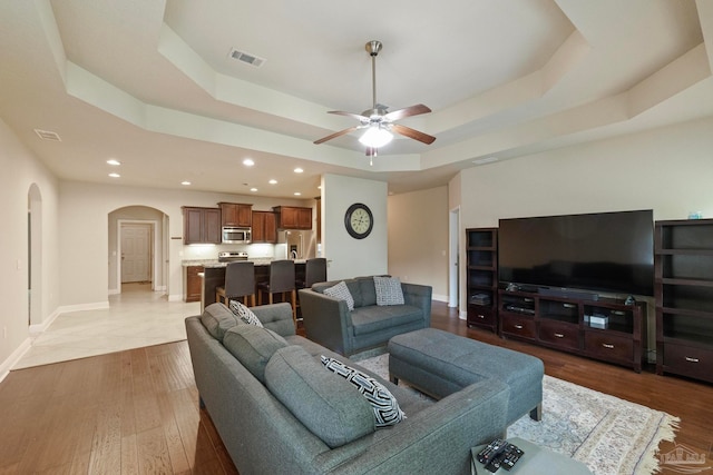 living room featuring a raised ceiling, ceiling fan, and light hardwood / wood-style floors