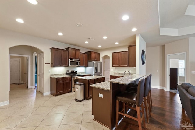 kitchen featuring a kitchen breakfast bar, light stone counters, kitchen peninsula, light hardwood / wood-style floors, and appliances with stainless steel finishes