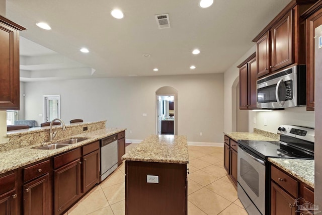 kitchen with a center island, sink, light stone countertops, and stainless steel appliances