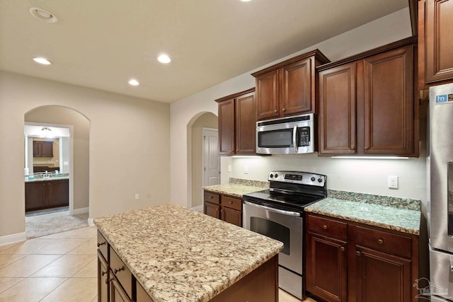 kitchen featuring light stone countertops, appliances with stainless steel finishes, a kitchen island, and light tile patterned flooring