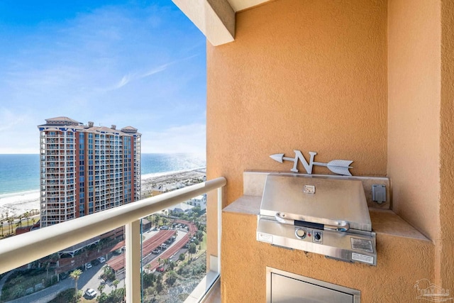 balcony featuring grilling area, a water view, an outdoor kitchen, and a view of the beach