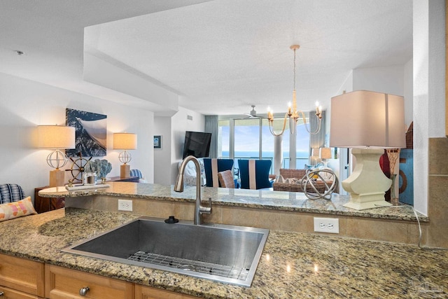 kitchen with a textured ceiling, a notable chandelier, stone counters, and a sink