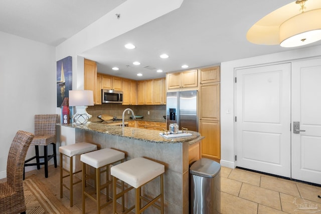 kitchen with stone counters, a breakfast bar, a peninsula, stainless steel appliances, and backsplash
