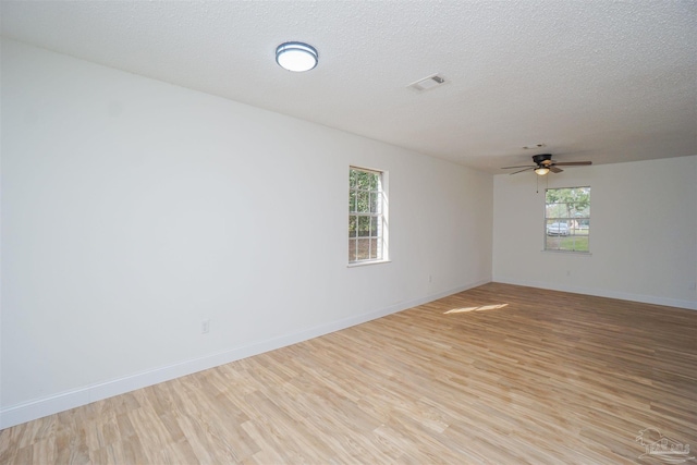 spare room with ceiling fan, light hardwood / wood-style floors, a textured ceiling, and a wealth of natural light