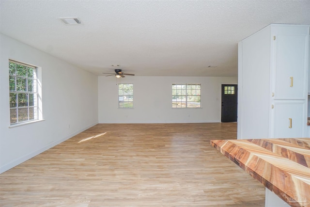 unfurnished living room with ceiling fan, light hardwood / wood-style flooring, a healthy amount of sunlight, and a textured ceiling