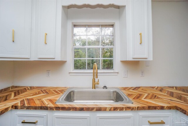 kitchen with wood counters, white cabinetry, and sink