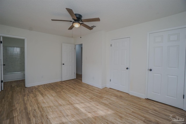 unfurnished bedroom with two closets, ensuite bathroom, ceiling fan, a textured ceiling, and light hardwood / wood-style floors