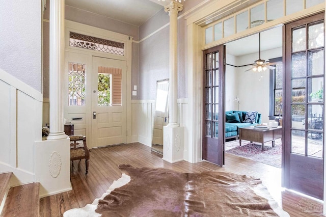 entryway with a wainscoted wall, a decorative wall, ceiling fan, wood finished floors, and ornate columns