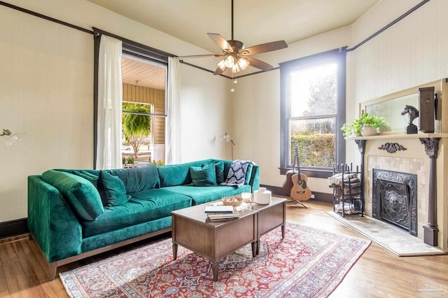 living area featuring ceiling fan, a fireplace, baseboards, and wood finished floors