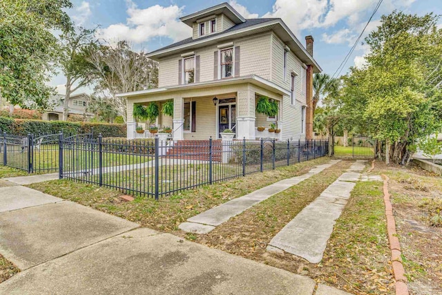 american foursquare style home featuring covered porch, a fenced front yard, a front yard, and a gate