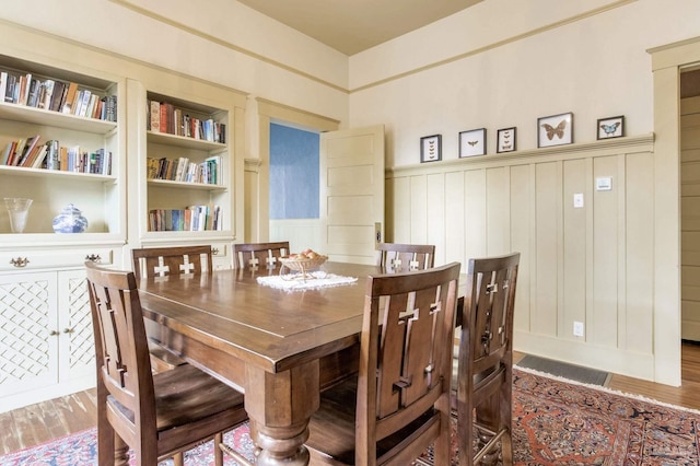 dining room featuring a wainscoted wall, wood finished floors, visible vents, and built in features