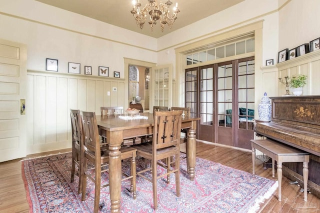 dining area featuring a wainscoted wall, wood finished floors, french doors, a decorative wall, and a notable chandelier