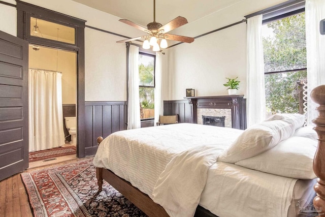 bedroom featuring wood finished floors, a wainscoted wall, ensuite bath, and multiple windows