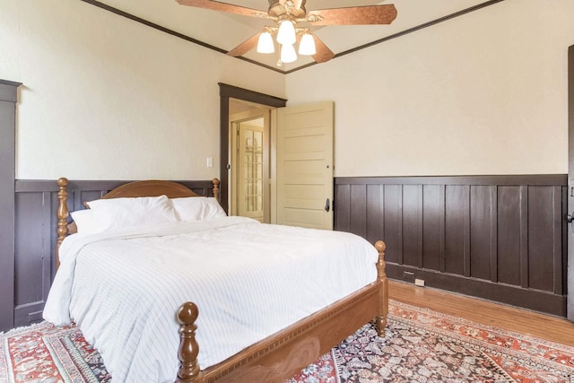 bedroom with light wood-type flooring, a wainscoted wall, ceiling fan, and ornamental molding