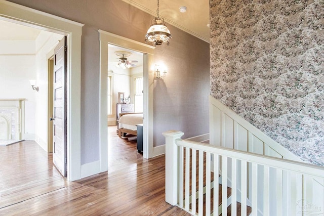 hallway featuring wainscoting, wood finished floors, crown molding, an upstairs landing, and a decorative wall