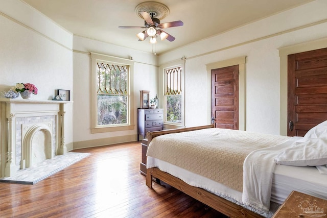 bedroom featuring baseboards, a ceiling fan, hardwood / wood-style floors, crown molding, and a fireplace