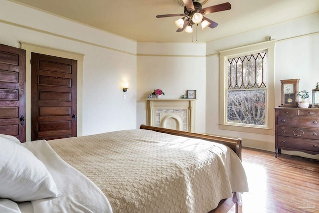 bedroom featuring a fireplace, a ceiling fan, and wood finished floors