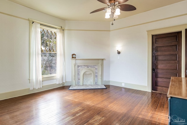 unfurnished living room with a ceiling fan, a fireplace with raised hearth, baseboards, and hardwood / wood-style flooring