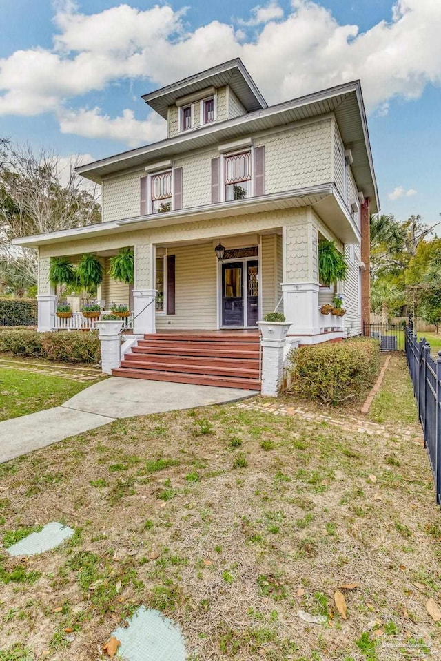 traditional style home with a porch, fence, a front lawn, and central AC unit