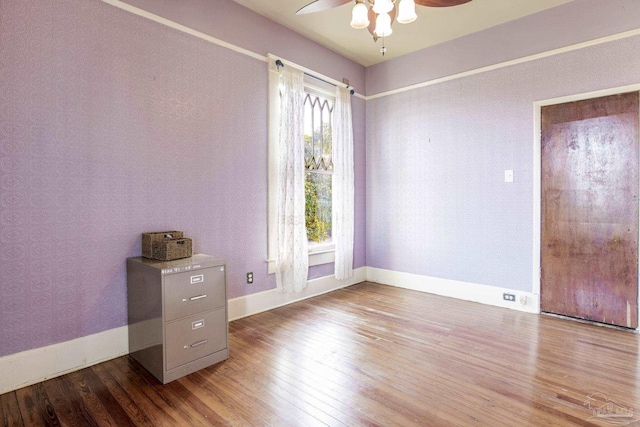 empty room featuring wood-type flooring, baseboards, and wallpapered walls