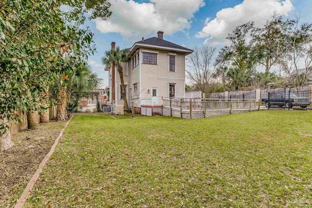 back of house featuring a fenced backyard, a chimney, a wooden deck, and a yard