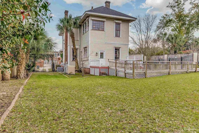 back of house featuring a deck, a lawn, a chimney, and a fenced backyard