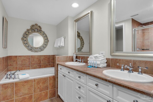 bathroom featuring a relaxing tiled tub and double sink vanity