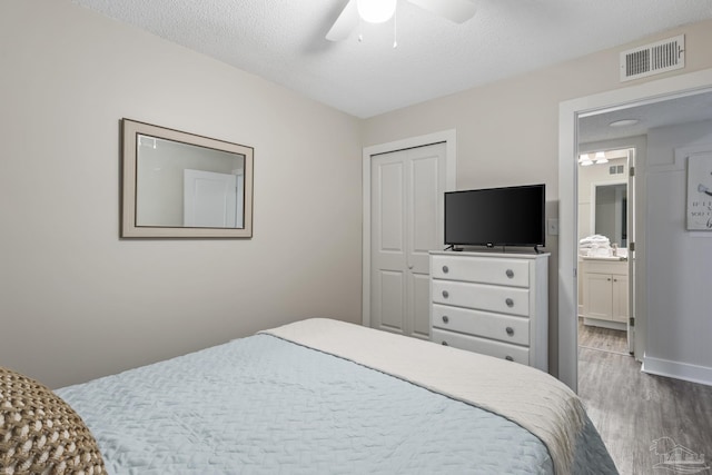 bedroom featuring ceiling fan, connected bathroom, light hardwood / wood-style floors, a textured ceiling, and a closet