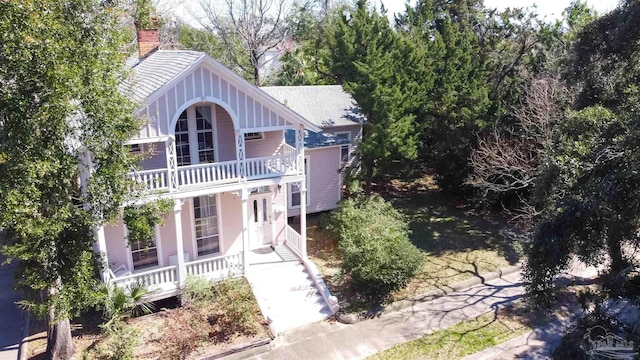 view of front facade featuring a balcony, covered porch, and a chimney