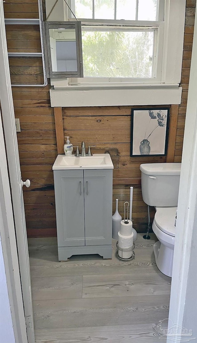 bathroom featuring toilet, wooden walls, a sink, and wood finished floors