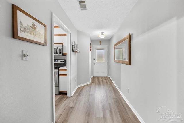 corridor with a textured ceiling and light hardwood / wood-style flooring