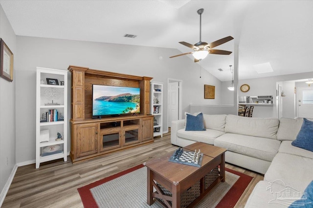 living room featuring vaulted ceiling with skylight, ceiling fan, and hardwood / wood-style floors