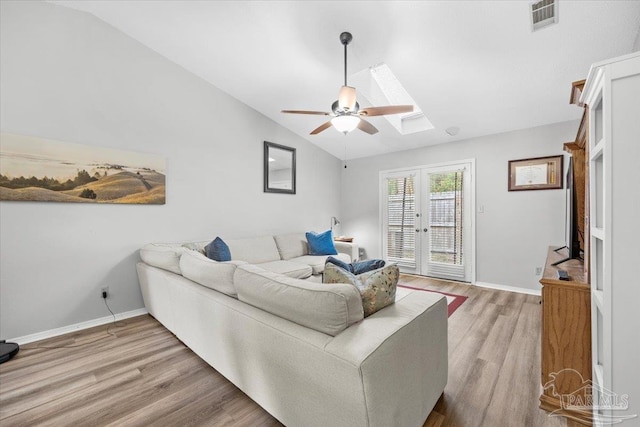 living room featuring hardwood / wood-style floors, ceiling fan, lofted ceiling with skylight, and french doors